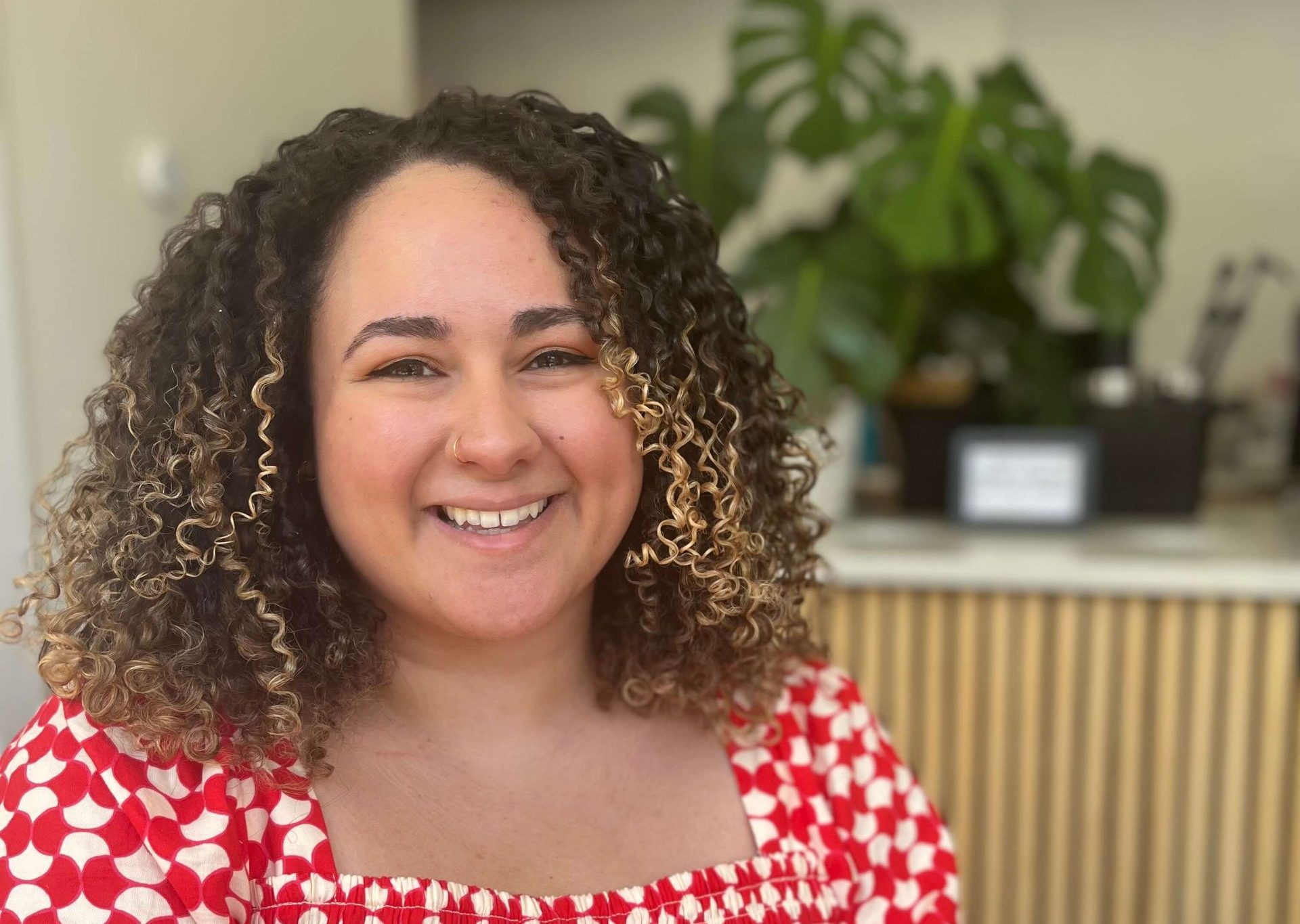 A smiling woman with curly hair in a red polka dot dress.