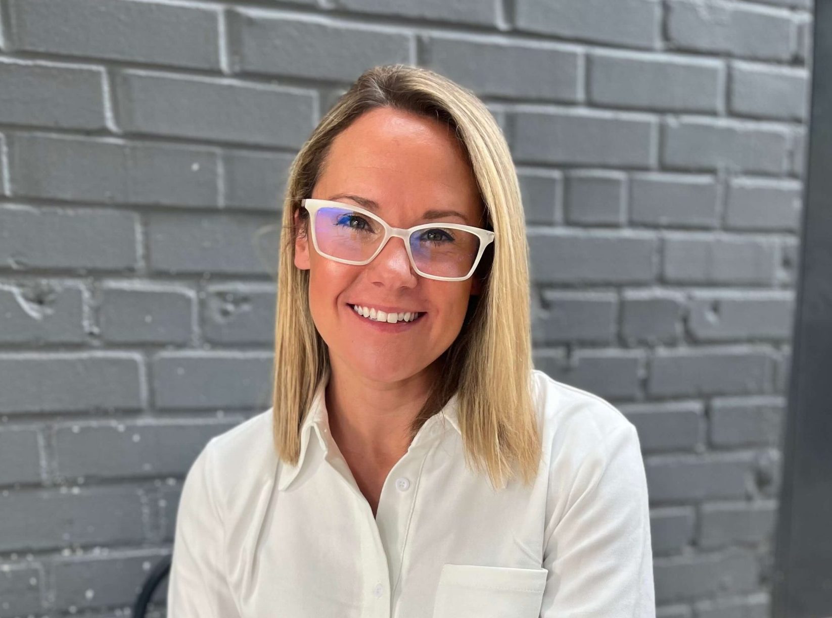 A woman wearing glasses in front of a brick wall.