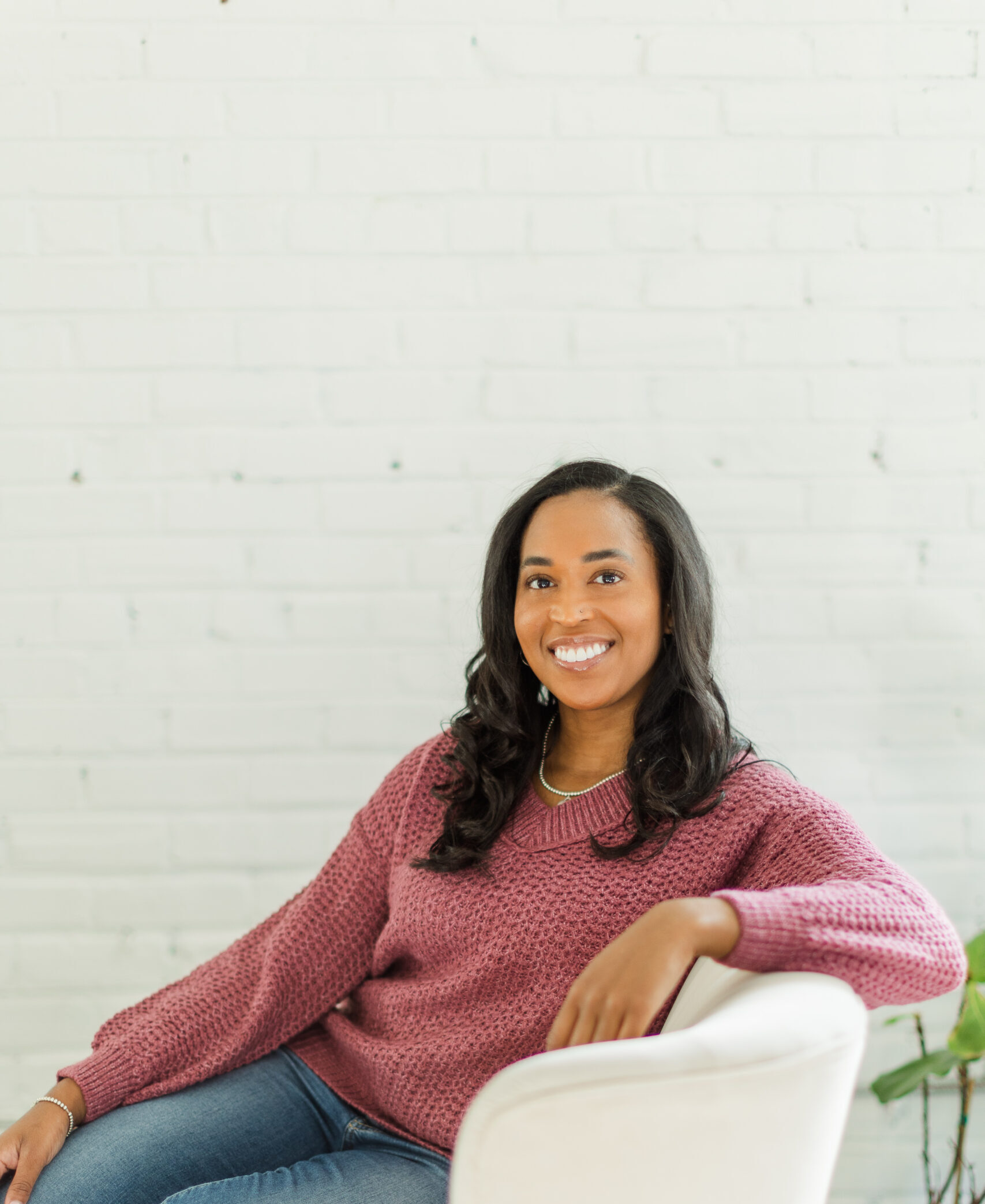 Woman smiling and sitting on a couch with a pink sweater