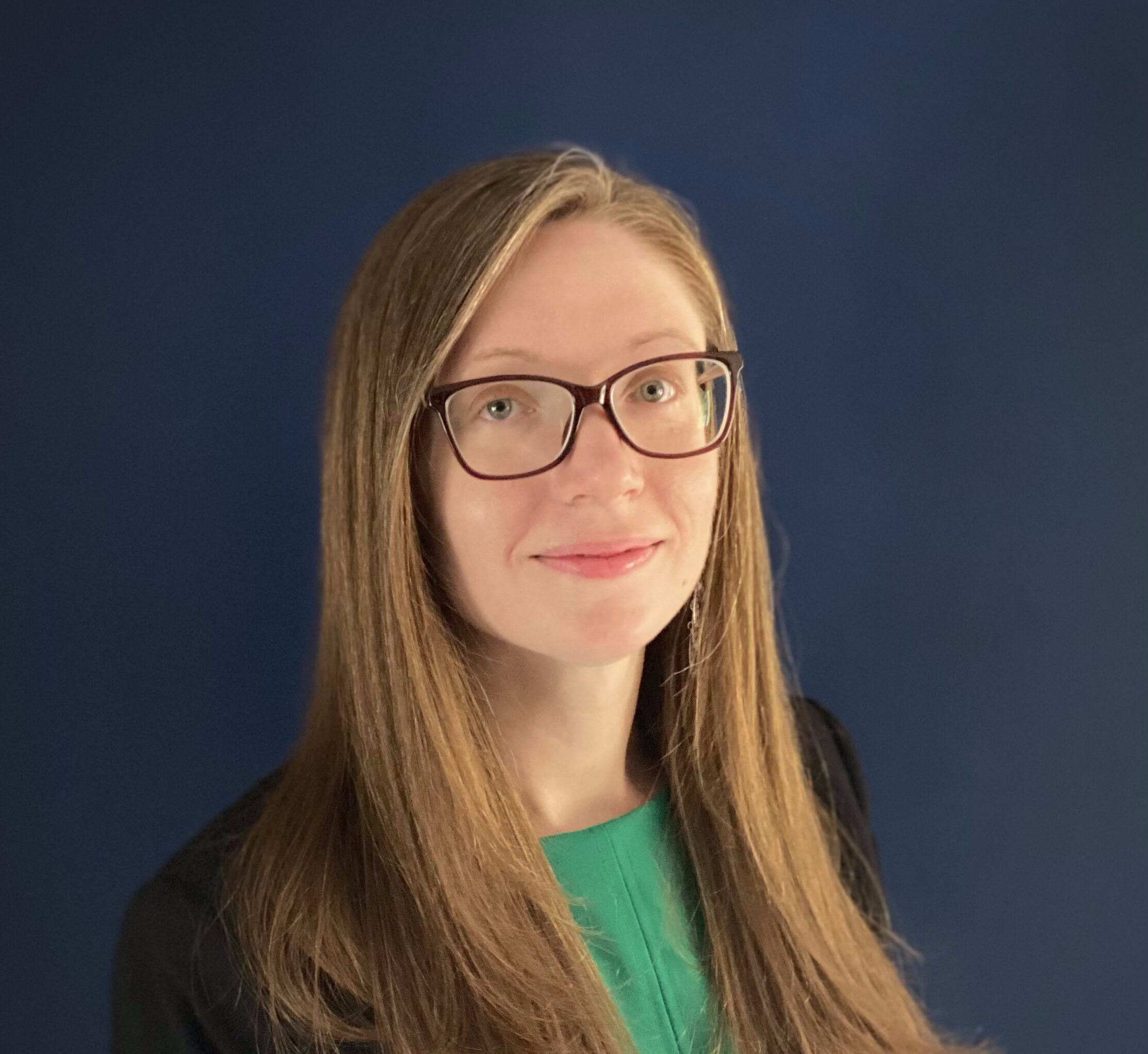 Woman with glasses smiling and wearing a green blouse